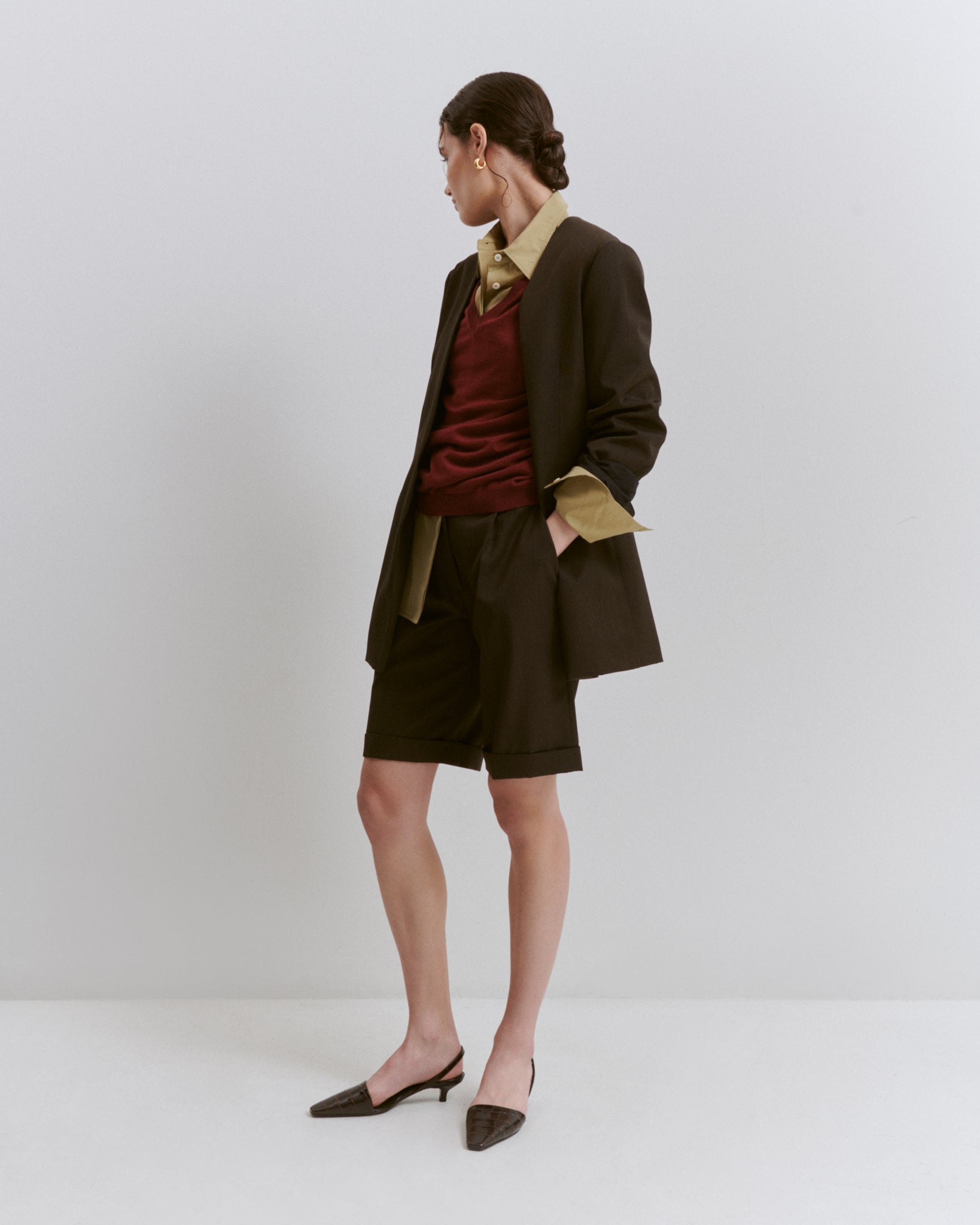 model wears Issue Twelve brown wool shorts and blazer with green shirt and red jumper