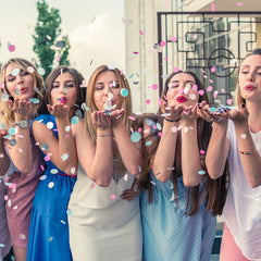 An image of a group of women blowing confetti at the camera.