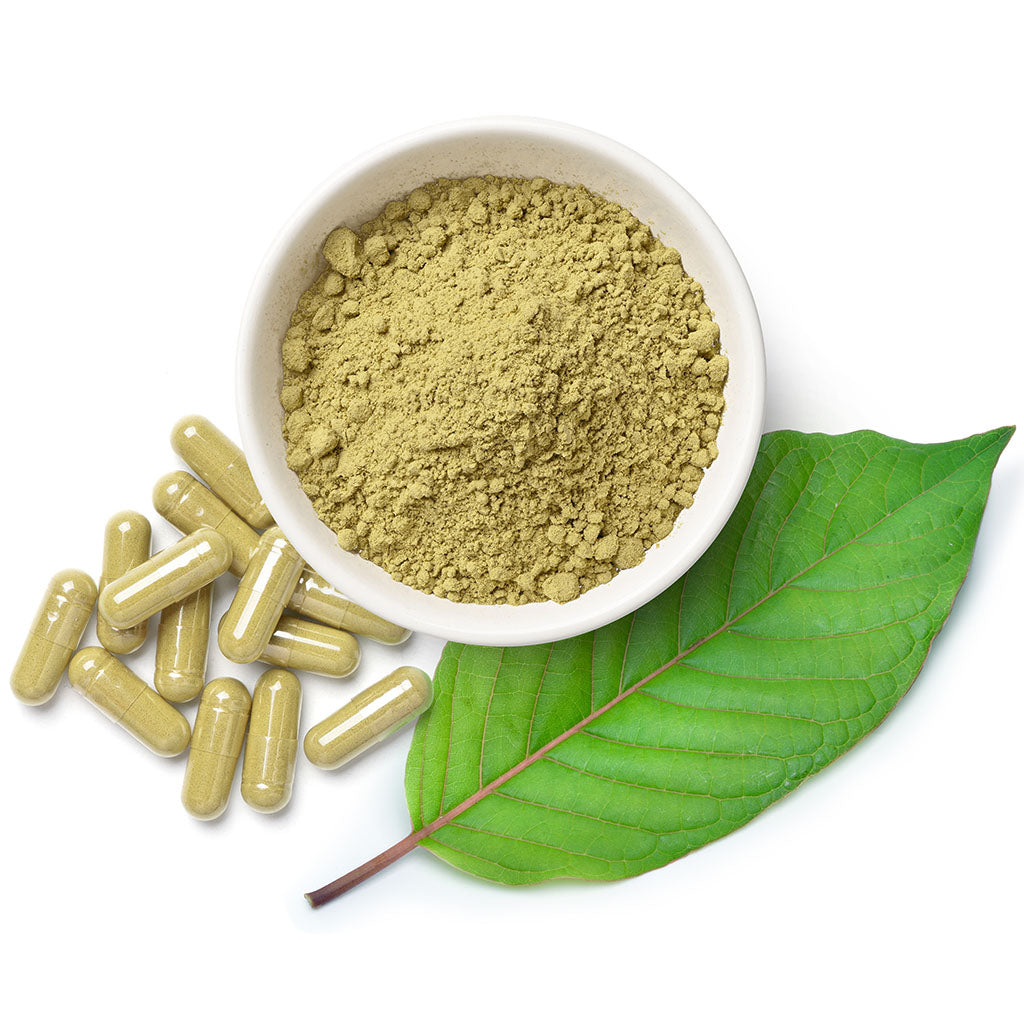 Photographic image depicting a bowl of kratom powder sitting next to a few Kratom Capsules, and a small bundle of raw kratom leaves. The image is a downward view, and sits on a stark white background.
