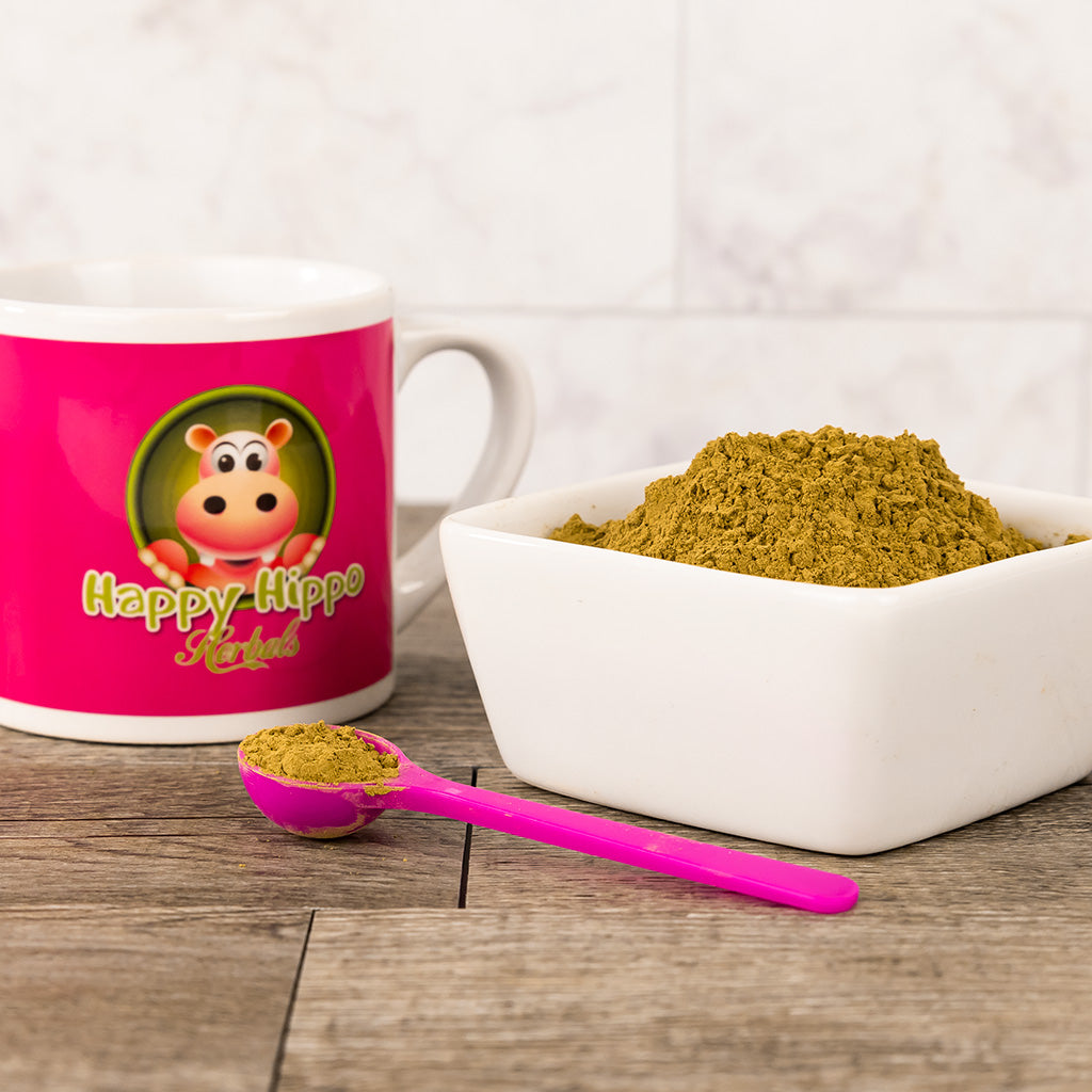 Photographic image depicting a Happy Hippo brand coffee cup sitting next to a white bowl of loose Yellow Maeng Da Kratom Powder. In front of the bowl is a 1gram little pink measuring scoop filled with yellow vein kratom powder.