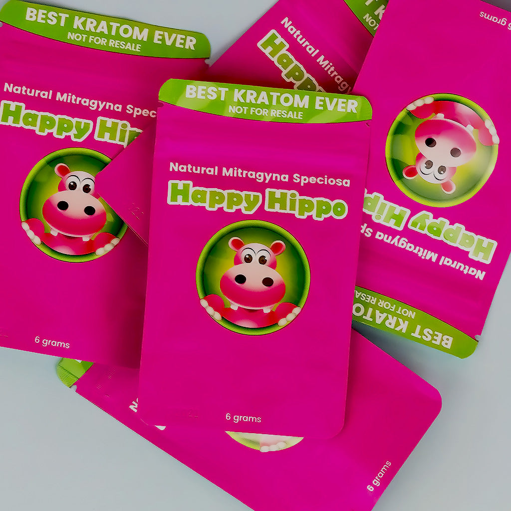 Photographic image depicting an assortment of Happy Hippo brand kratom powder packets. The packets each contain 6 grams of kratom powder, have pink trade dress and feature the Happy Hippo Herbals logo with Puddles the Hippo character at the center.