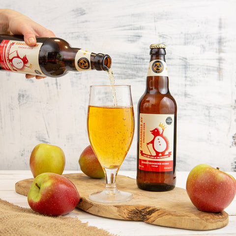 Cider being poured into a glass. Apples around the glass.