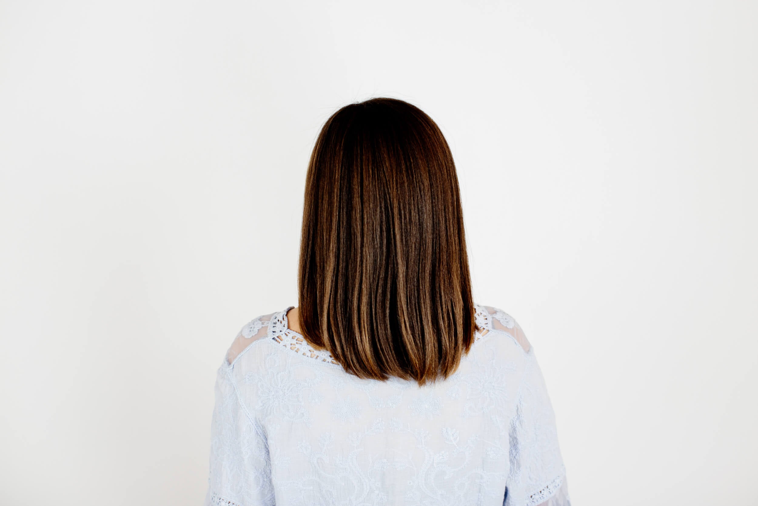 A woman shows the back of her hair that has been straightened.
