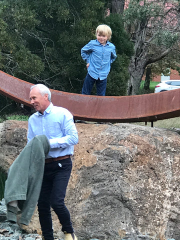 A child playing on a large crescent shaped metal sculpture, with a man in the foreground. 