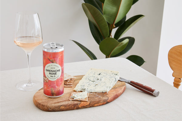 Canned Wine Co. Grenache Rosé next to a rosé wine glass, dolcelatte cheese and cheese knife