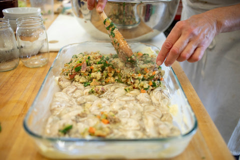 stuffing overtop of shucked oysters in a clear glass baking dish