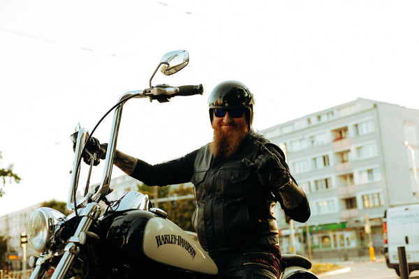 Smiling bearded man in leather vest riding Harley-Davidson motorcycle in urban setting