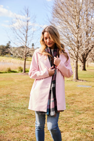 Woman standing in a field wearing a light pink collared coat.