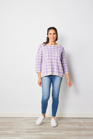 Woman wearing lilac gingham sweater and blue jeans.