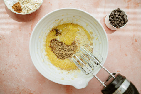 ingredients in bowl with hand mixer resting on side of bowl