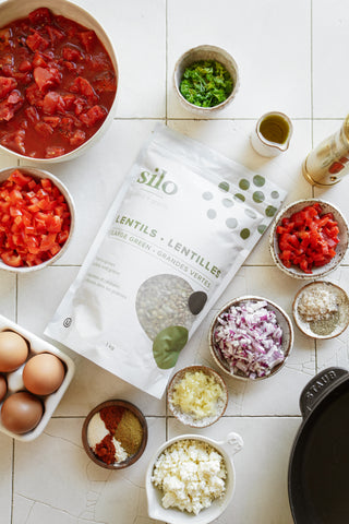 a package of Silo large green lentils surrounded by a rainbow of spices, diced tomatoes, red peppers and eggs