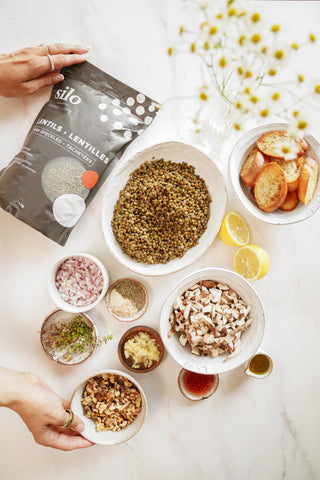 A package of Silo Dark Speckled Lentils beside dishes full of mushrooms, colourful nuts, spices and onions