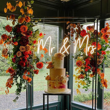 Snow white Mr and Mrs wedding neon sign and orange flowers and cake.jpg__PID:e8fdd379-4f11-437f-a82e-e5ad513278ab