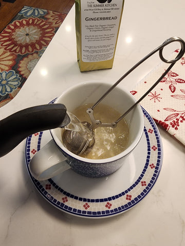 a tea cup with a snap mesh tea ball in it with hot water being poured over top