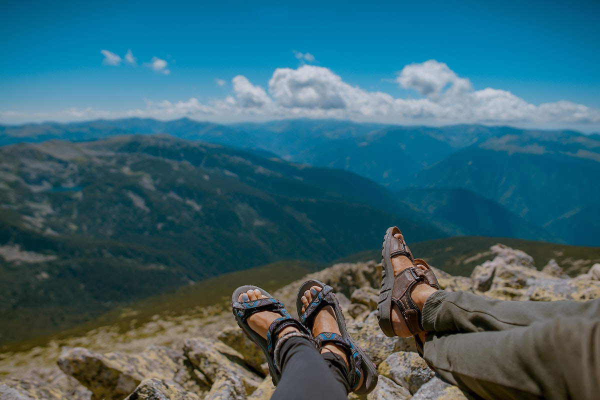 two people's feet in hiking sandles looking out into a mountain valley