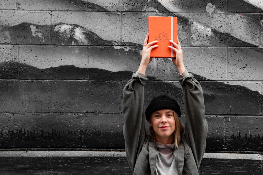 blonde woman holding up a mindful travel journal