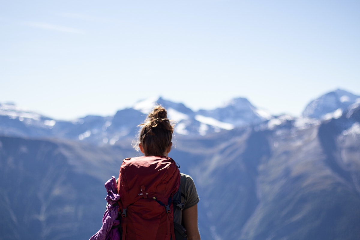 girl with a red backpack with her back faced away looking at snowy mountains