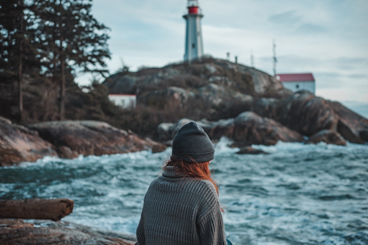 a red headed girl standing by the ocean and a lighthouse