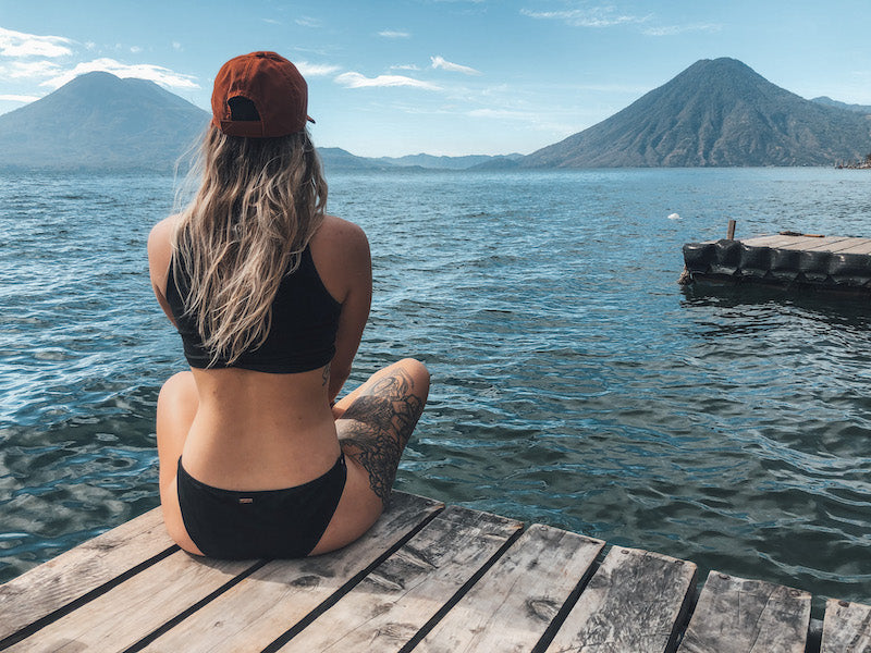 young woman sitting on a dock looking out over Lake Atitlan's volcanos