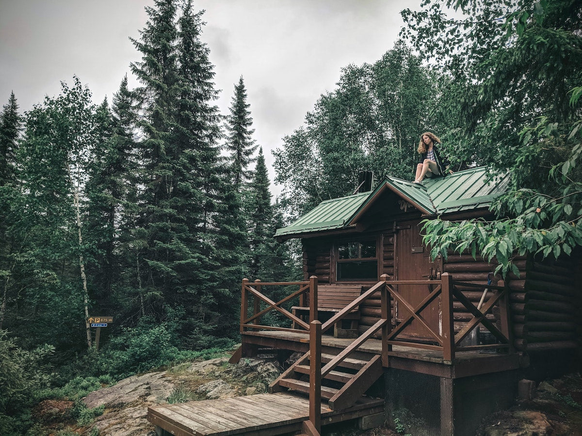 girl sitting on top of a cabin in the forest