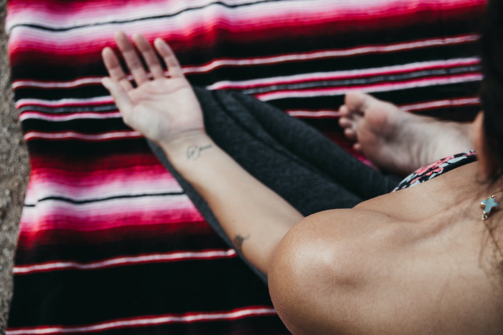 a woman meditating on a pink striped blanket