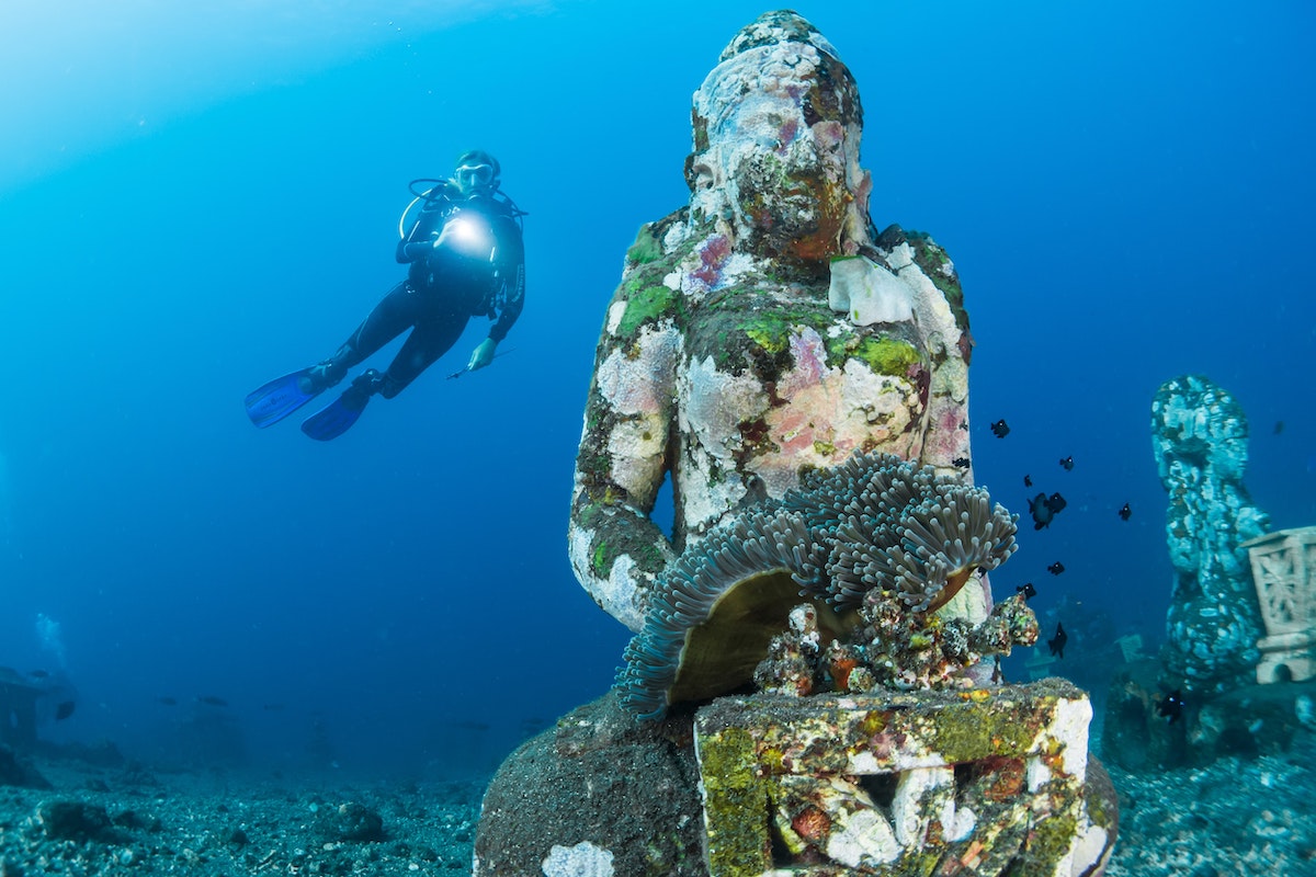 an underwater statue with a diver swimming behind in Bali, Indonesia
