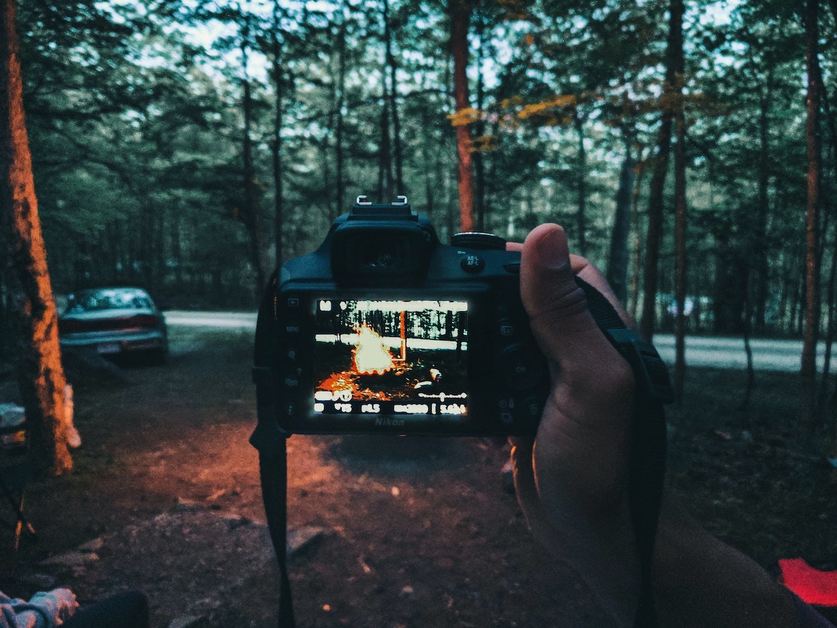 a hand holds a camera with a photo of a campfire on it