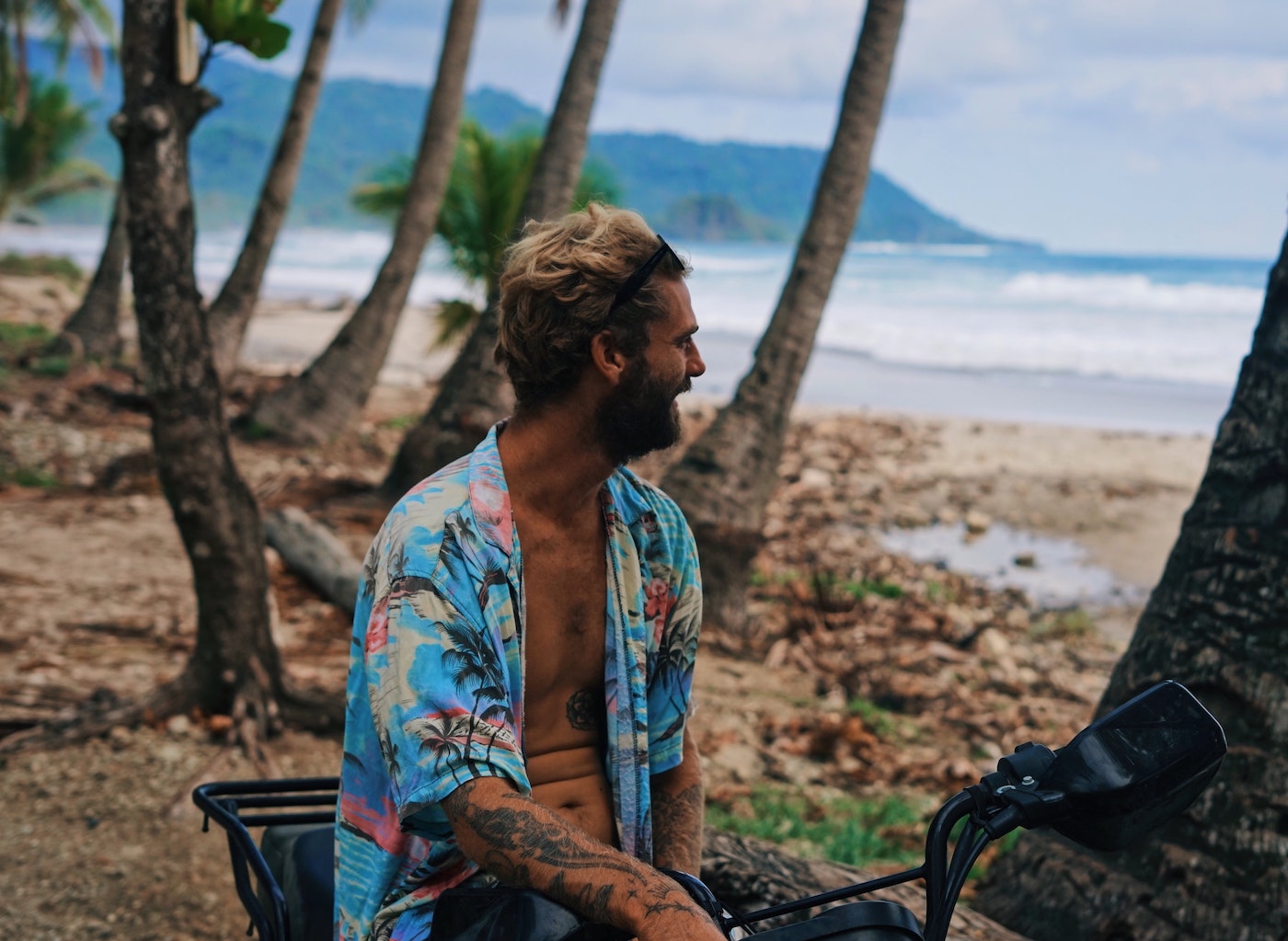 a man with tattoos sits on a motorbike on the beach