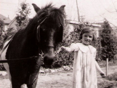 Black and white photo of a little girl playing with her pony, capturing a joyful childhood memory, with animals and nature.