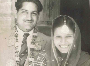 A black and white vintage photograph of a happy south Asian couple on their wedding day wearing traditional wedding outfits.