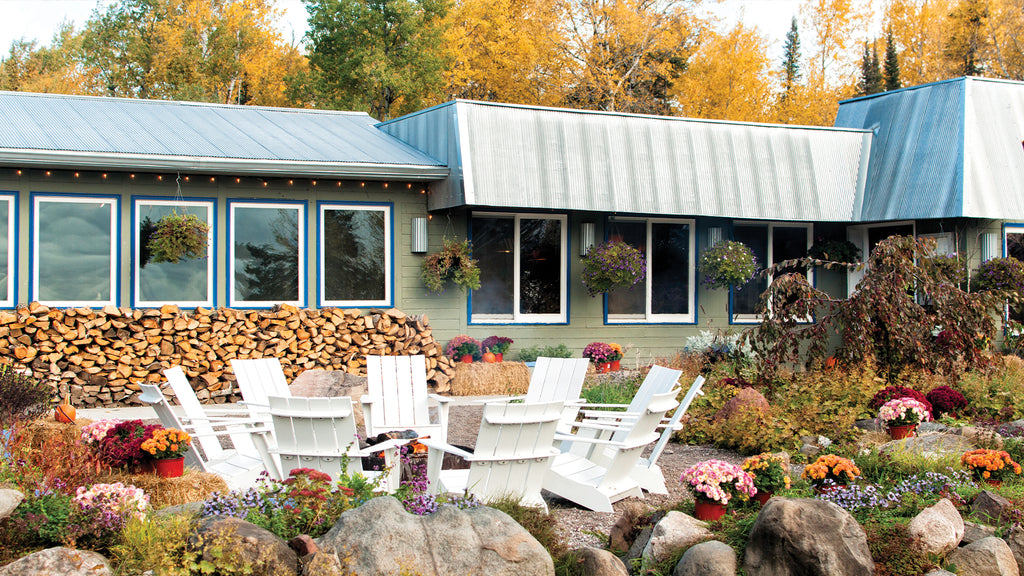 Image: Front view of New Scenic Cafe in fall. A set of six Adirondack Chairs in the Cloud White are set around a fire pit  in the front left portion of the image.