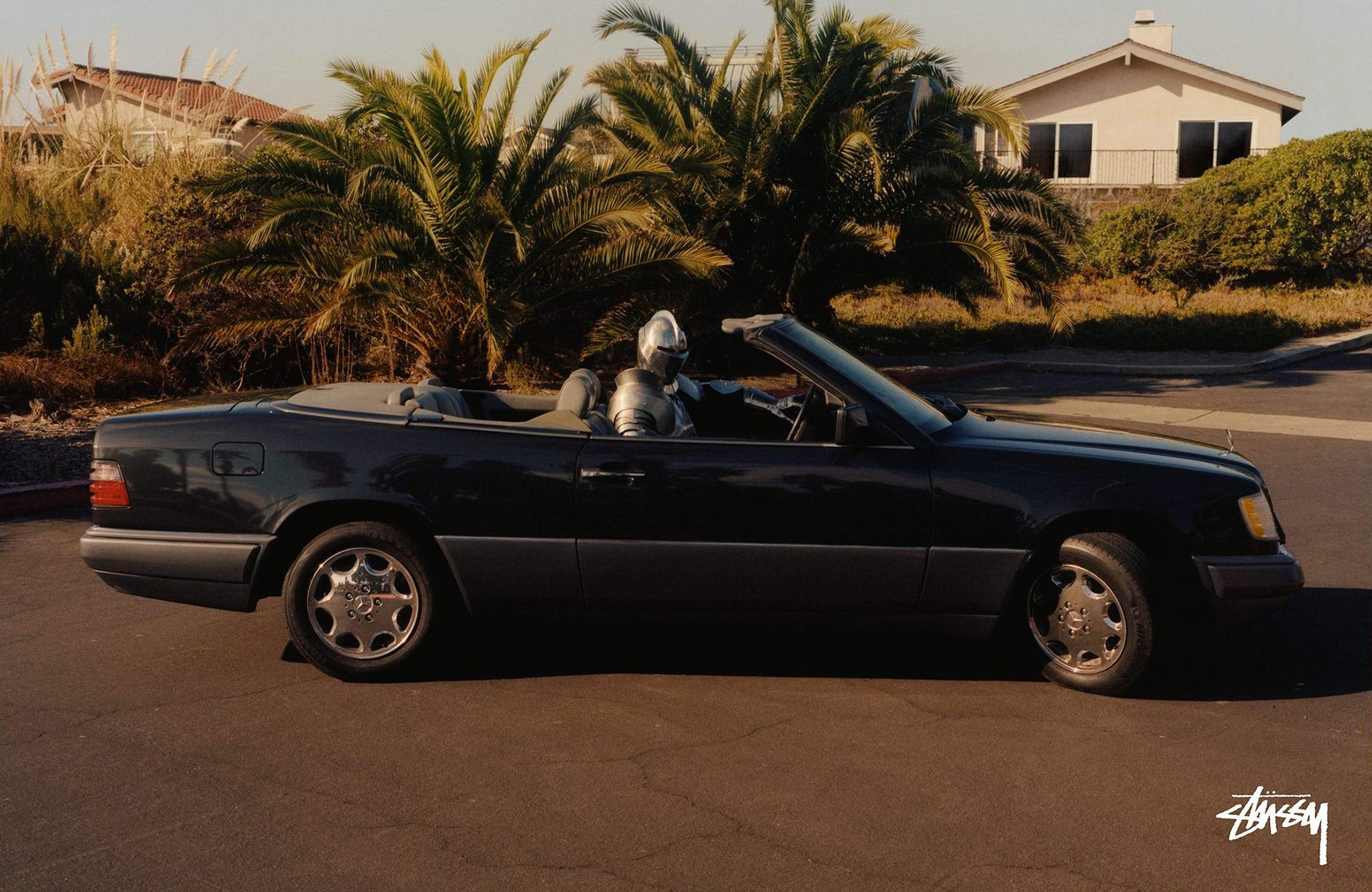 Person dressed in armor driving a black Mercedes SL parked in a cul-de-sac for Stussy photoshoot