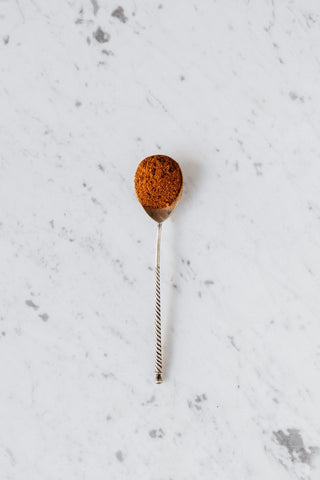 A spoonful of dark red kratom powder on a white background