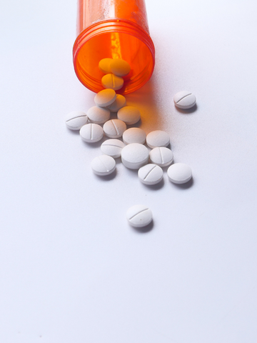 A bottle of white pills that may result in delta-11 drug interactions spilled from an orange prescription pill bottle. 