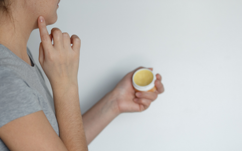 A woman for applying CBD salve to her jaw line to combat blemishes.