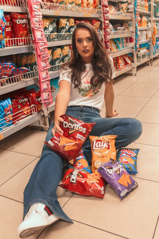 A woman sitting on the floor of a gas station with a lap full of snack options