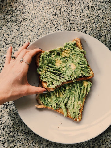 A person spreading CBD infused guacamole on two pieces of toast.