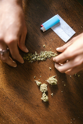 A person breaks down weed by hand by rolling it between their fingers until it reaches a fine consistency.