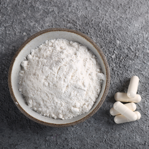 A bowl of L-theanine powder and some L-theanine capsules to show examples of forms of L-theanine that can be used for supplementing. 