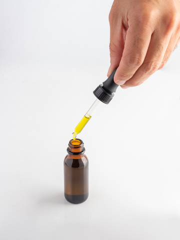 A person measuring a small dose of Delta-8-THC tincture from an amber bottle