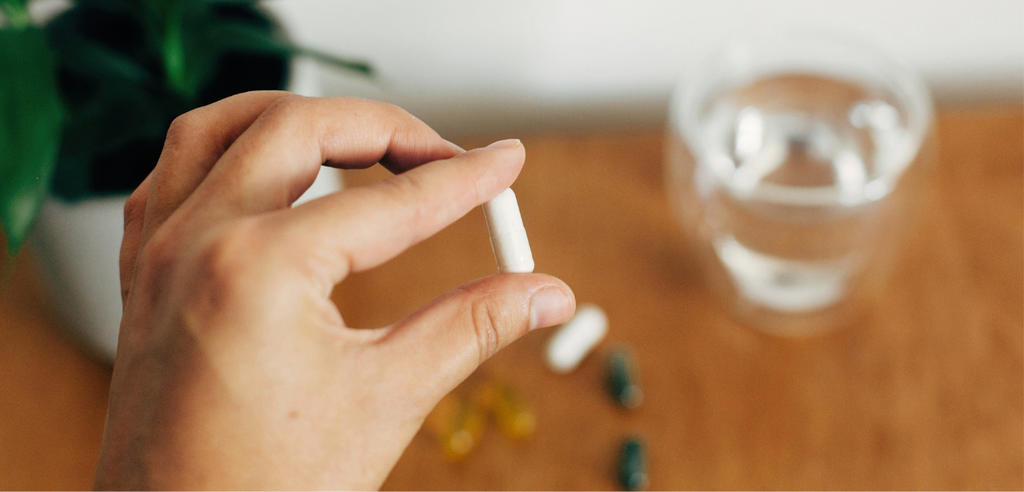 A person holding a single white supplement for improving sex drive near a glass of water