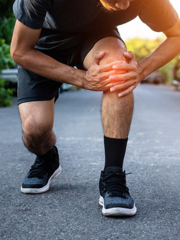 A man crouching and holding his inflamed knee due to tendonitis pain