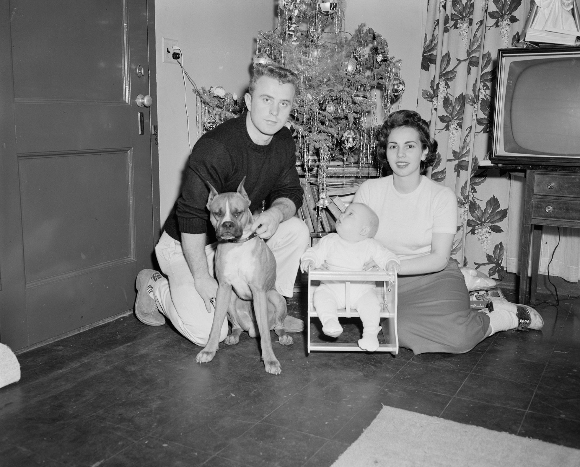 A vintage family portrait of a man and his wife, a newborn baby, and a dog.