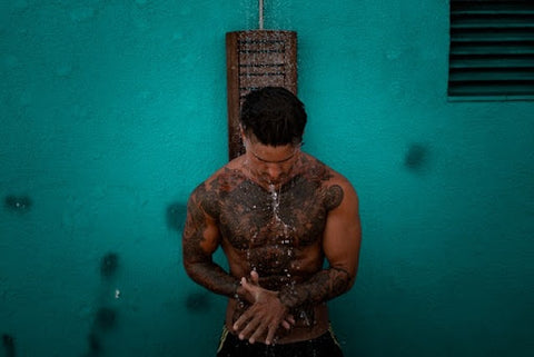 A man covered in tattoos taking a shower