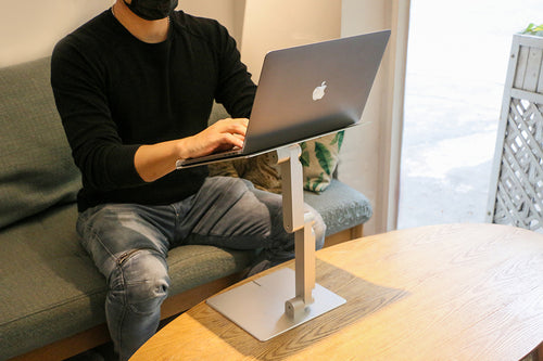 standing laptop holder, man sitting on sofa with macbook pro on laptop stand on desk, in cozy coffee shop