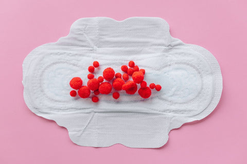 opened period pad with red cotton balls on it, as a mock appearance of blood