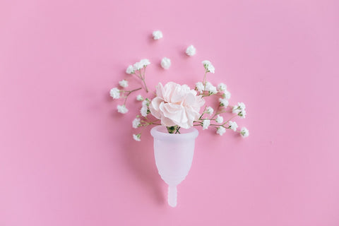 menstrual cup with white flower in it and smaller white flowers around it, on a pink background