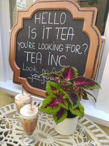 Tea Inc Sign reading 'Hello is it tea you're looking for' and two iced coffees on a patio table.