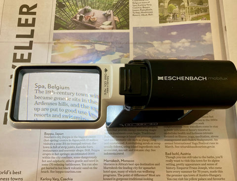 Eschenbach rectangular magnifier with a black handle, sitting on a newspaper