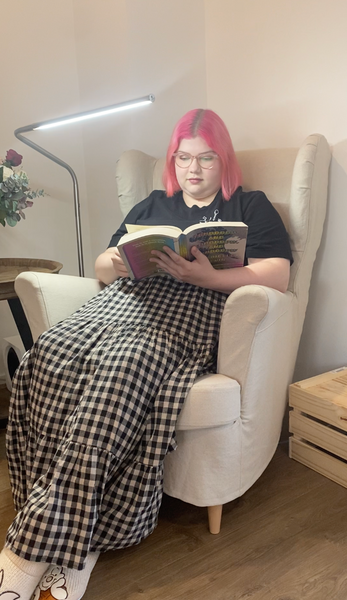 Young lady reading a novel in an arm chair, with the aid of a floorstand Daylight lamp